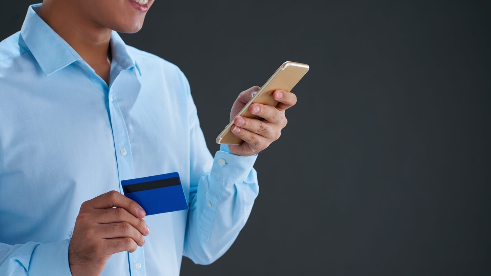 A man in a blue shirt holding a credit card and a phone