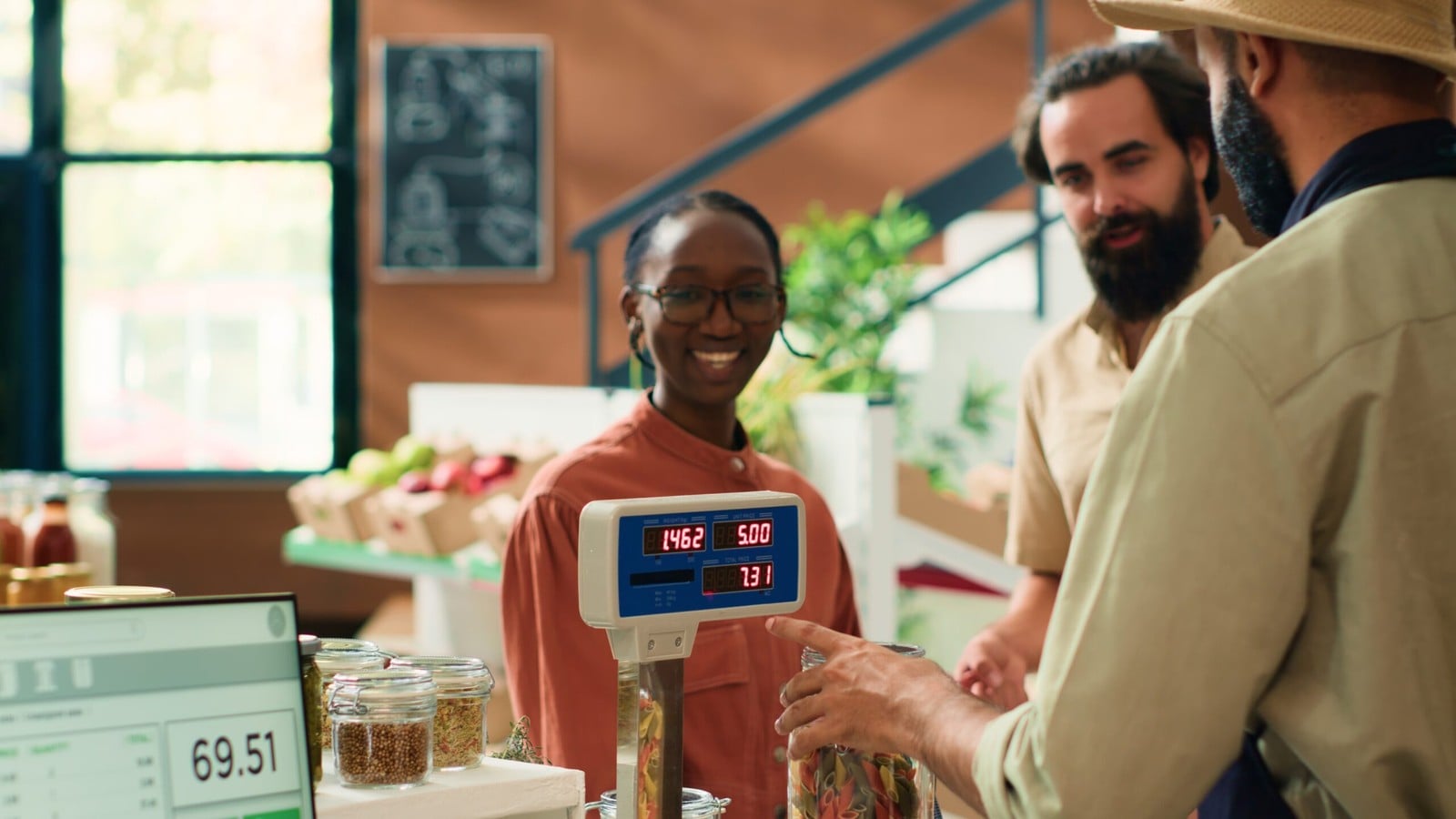 A shopkeeper weighing produce for two customers at a counter