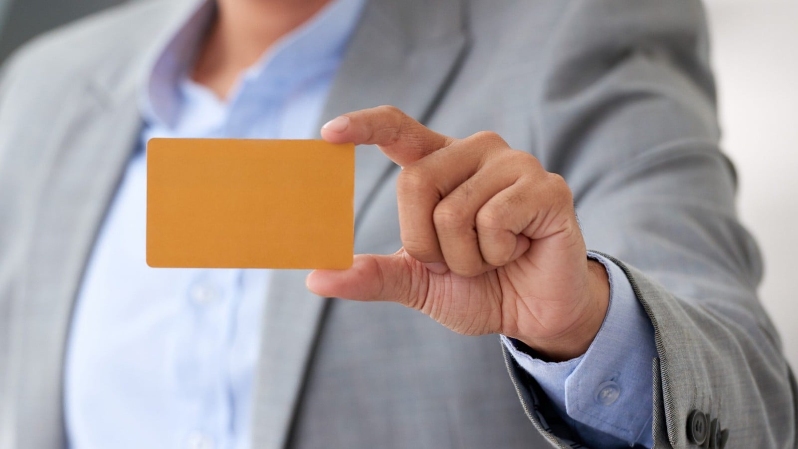 A hand in a grey suit holding an orange payment card