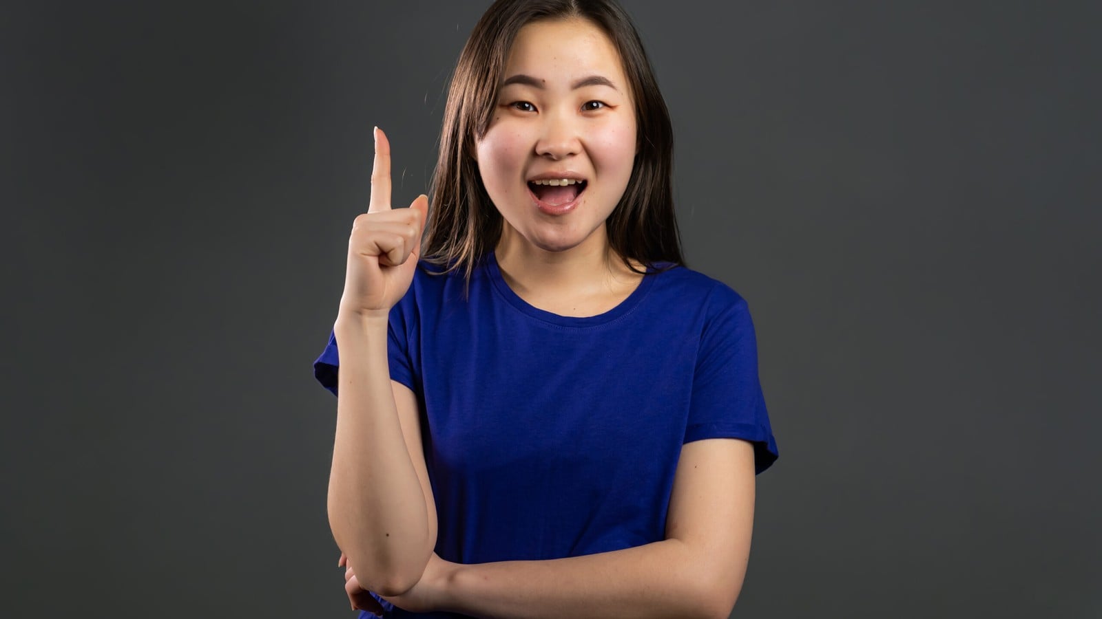 A woman in a blue shirt raising one finger against a dark grey background